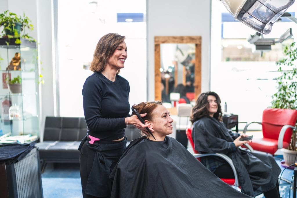 Smiling Hairdresser Adjusting Client's Hair at Salon